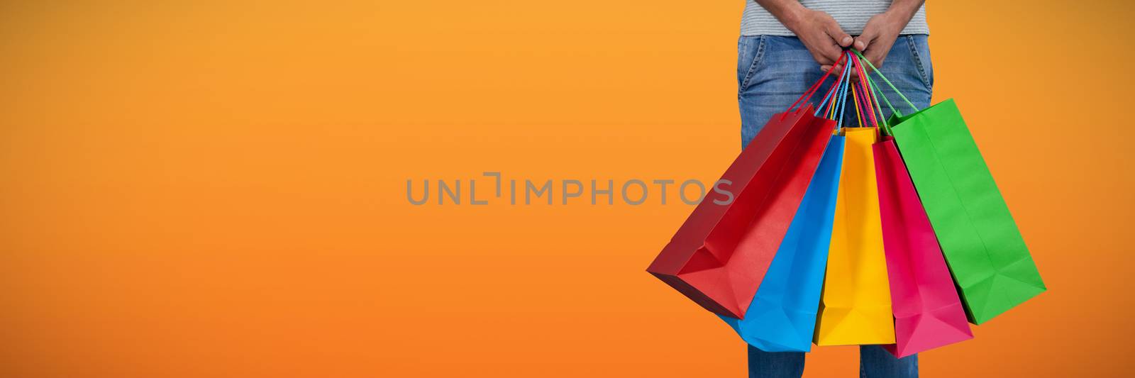 Low section of man carrying colorful shopping bag standing against white background against abstract saffron background