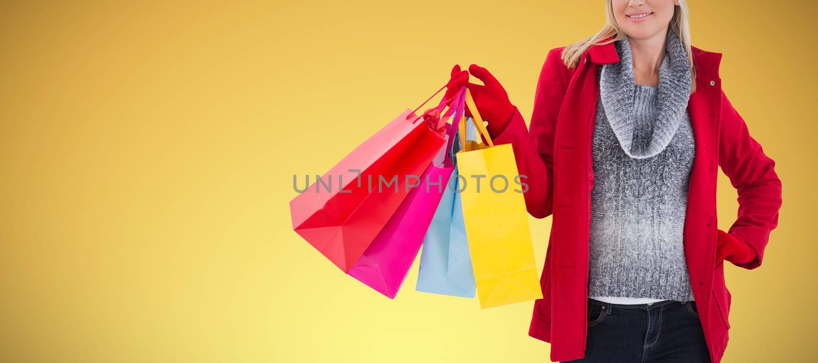 Blonde in winter clothes holding shopping bags against abstract yellow background