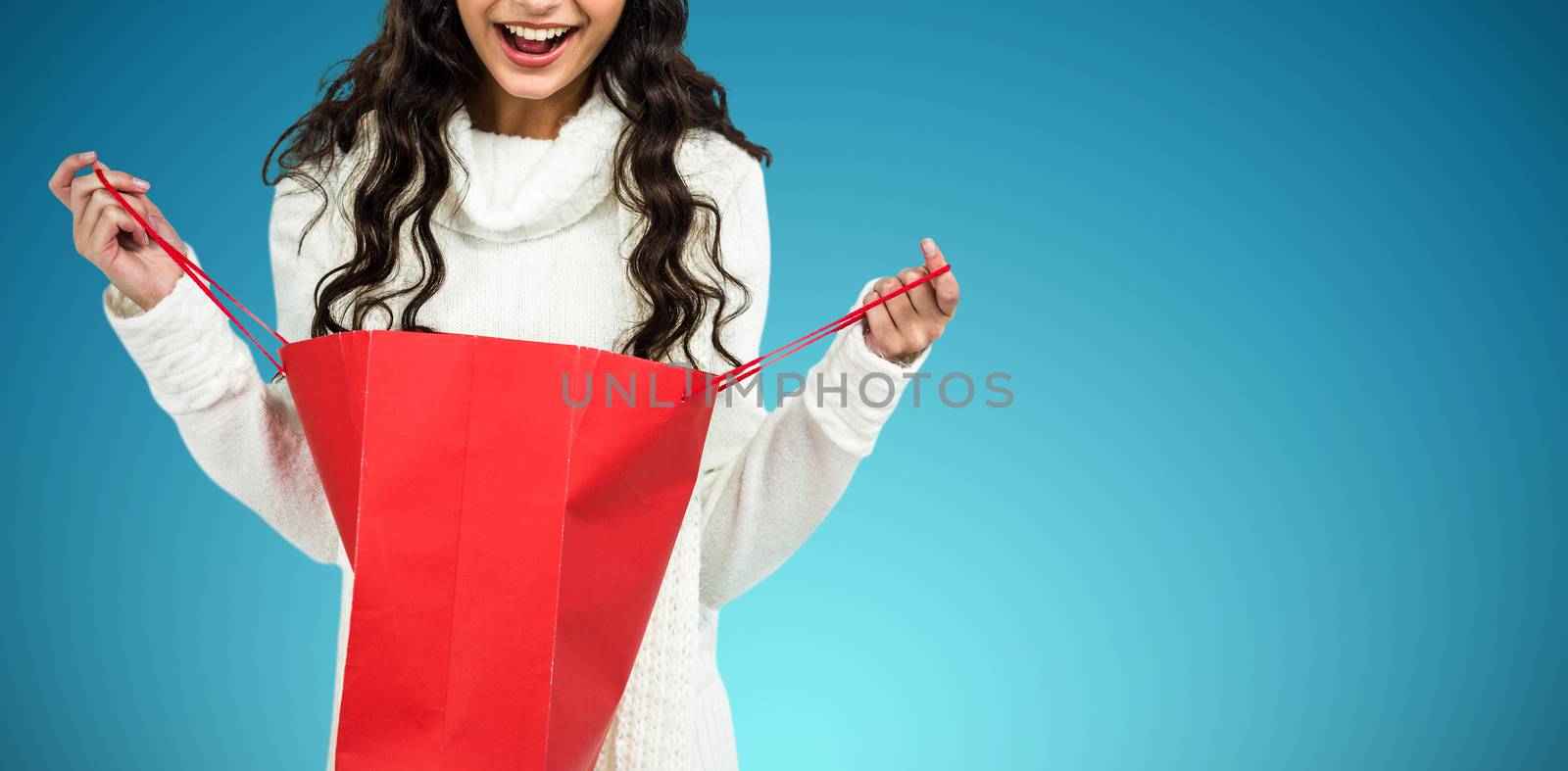 Happy woman with christmas hat opening red shopping bag against abstract blue background