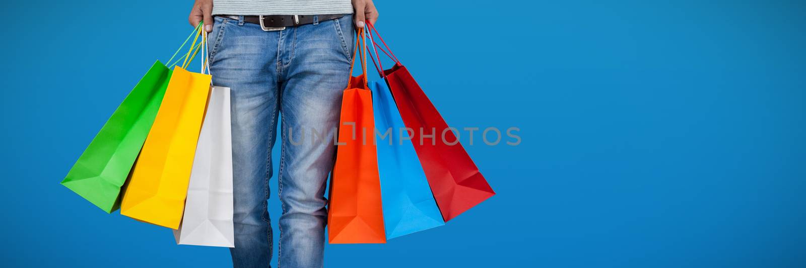 Low section of man carrying colorful shopping bag against abstract blue background