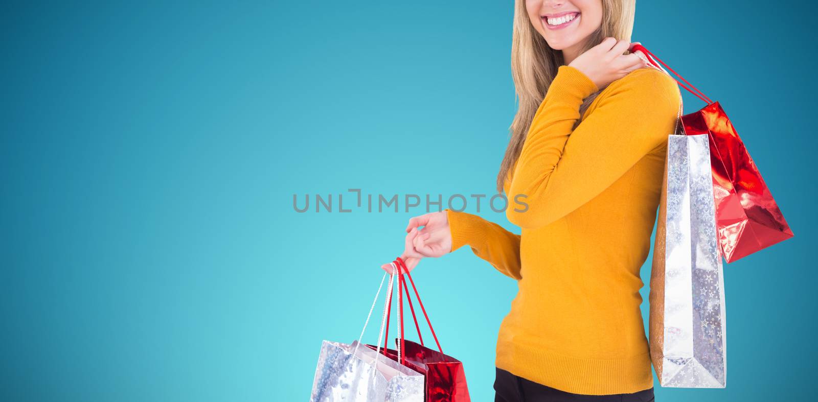 Stylish blonde smiling with shopping bags against abstract blue background