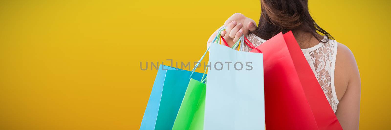 Rear view of brunette holding shopping bags against abstract mustard background