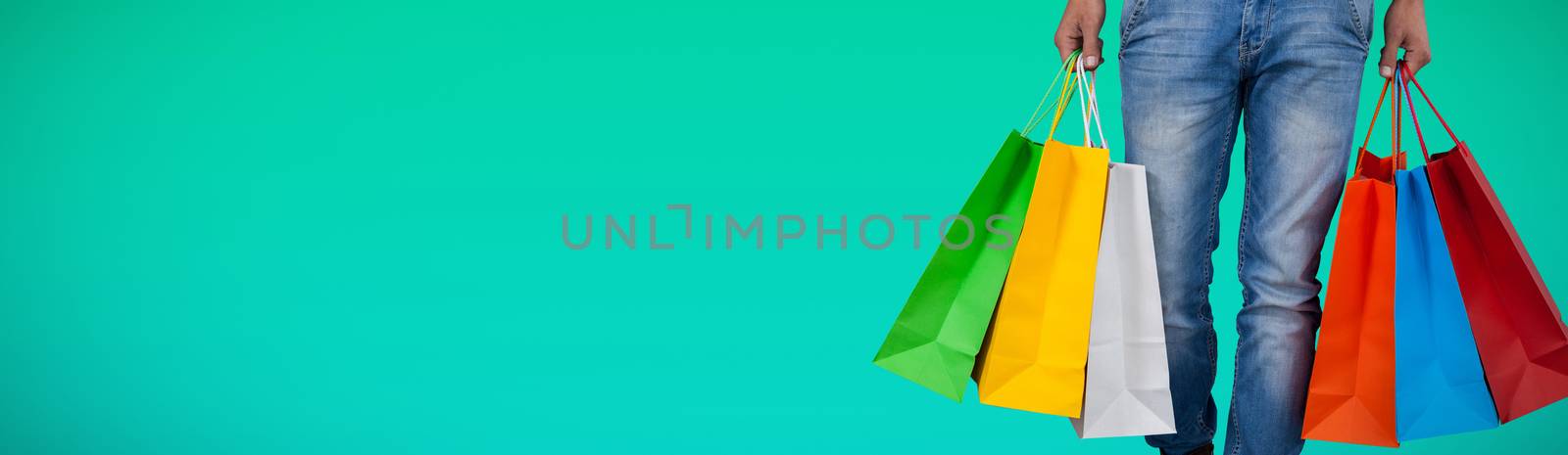 Low section of man carrying colorful shopping bag against white background against abstract green background
