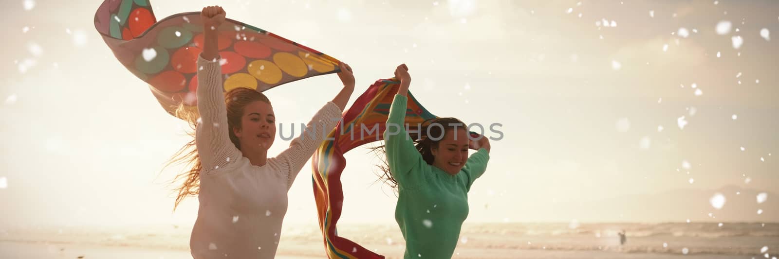 Snow falling against female friends running with towel on beach