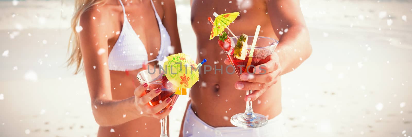 Snow falling against attractive young couple smiling at camera holding cocktails