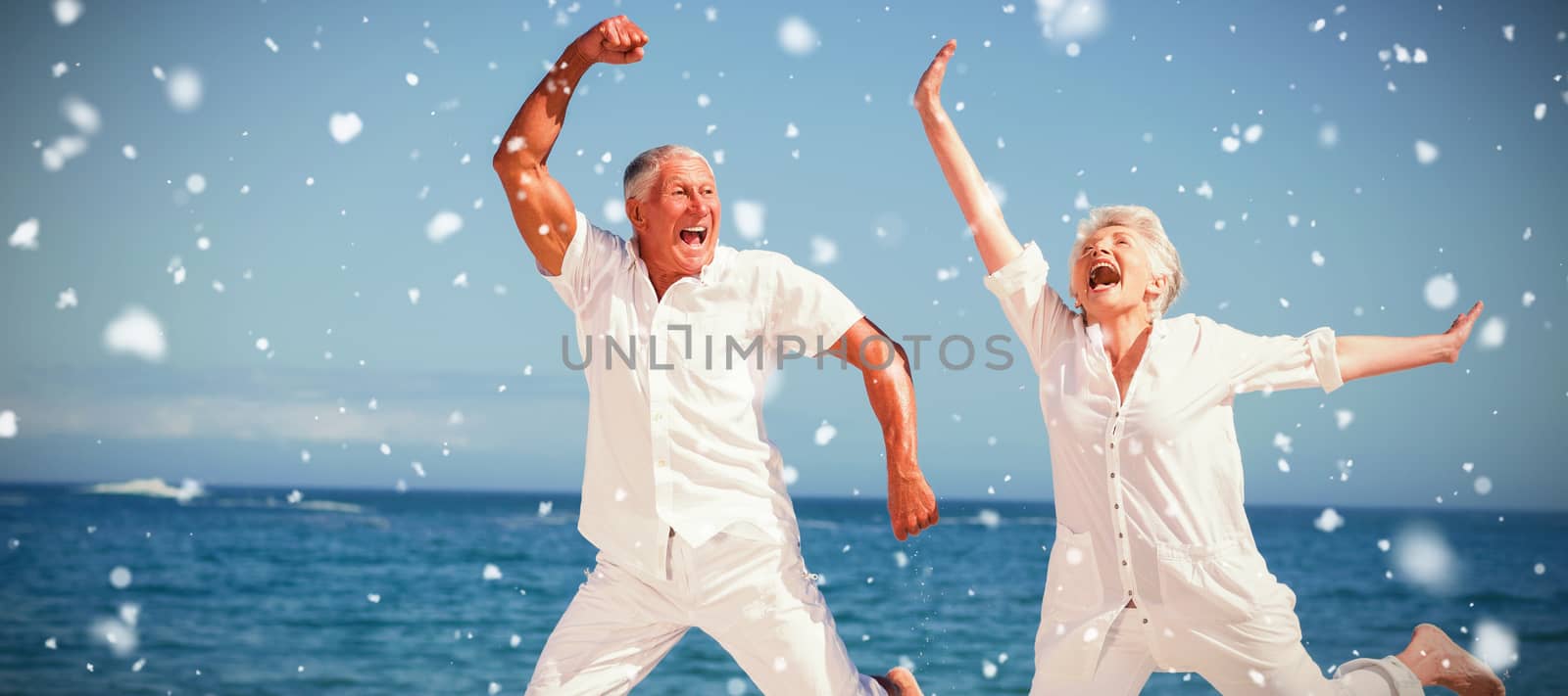 Snow falling against senior couple jumping at the beach