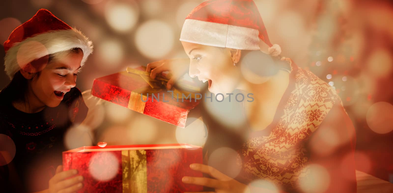 Festive mother and daughter opening a glowing christmas gift against light circles on black background