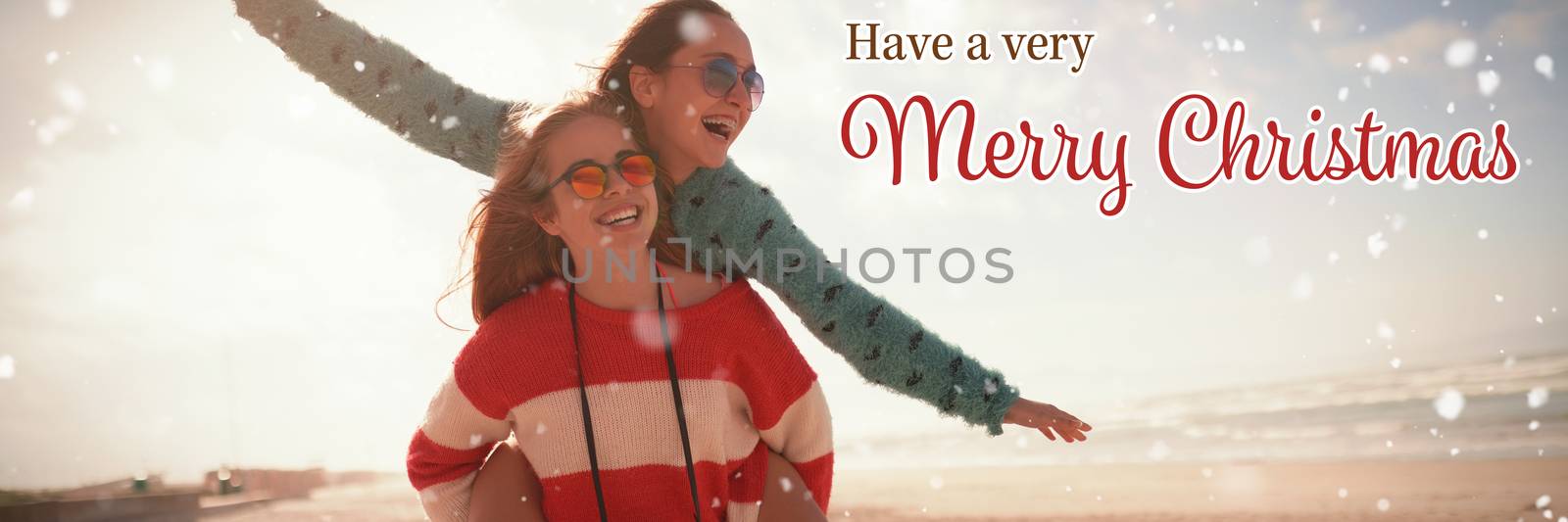 Christmas card against female best friends giving piggy back in beach