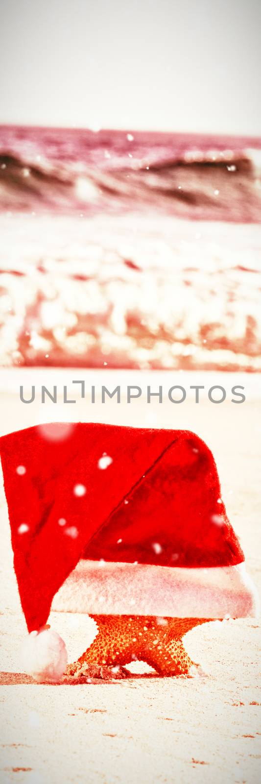 Snow falling against starfish with santa hat on beach