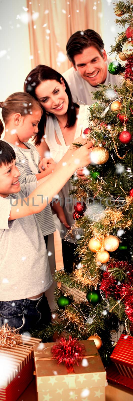 Happy family decorating a Christmas tree with boubles against snow falling
