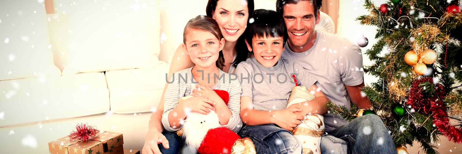 Happy family at Christmas time holding lots of presents against snow falling