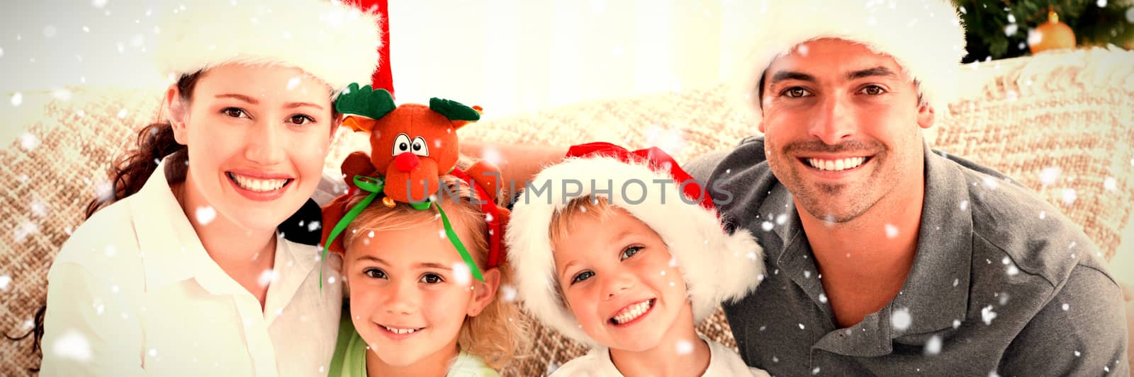 Portrait of a happy family with Christmas hats sitting on the sofa against snow falling