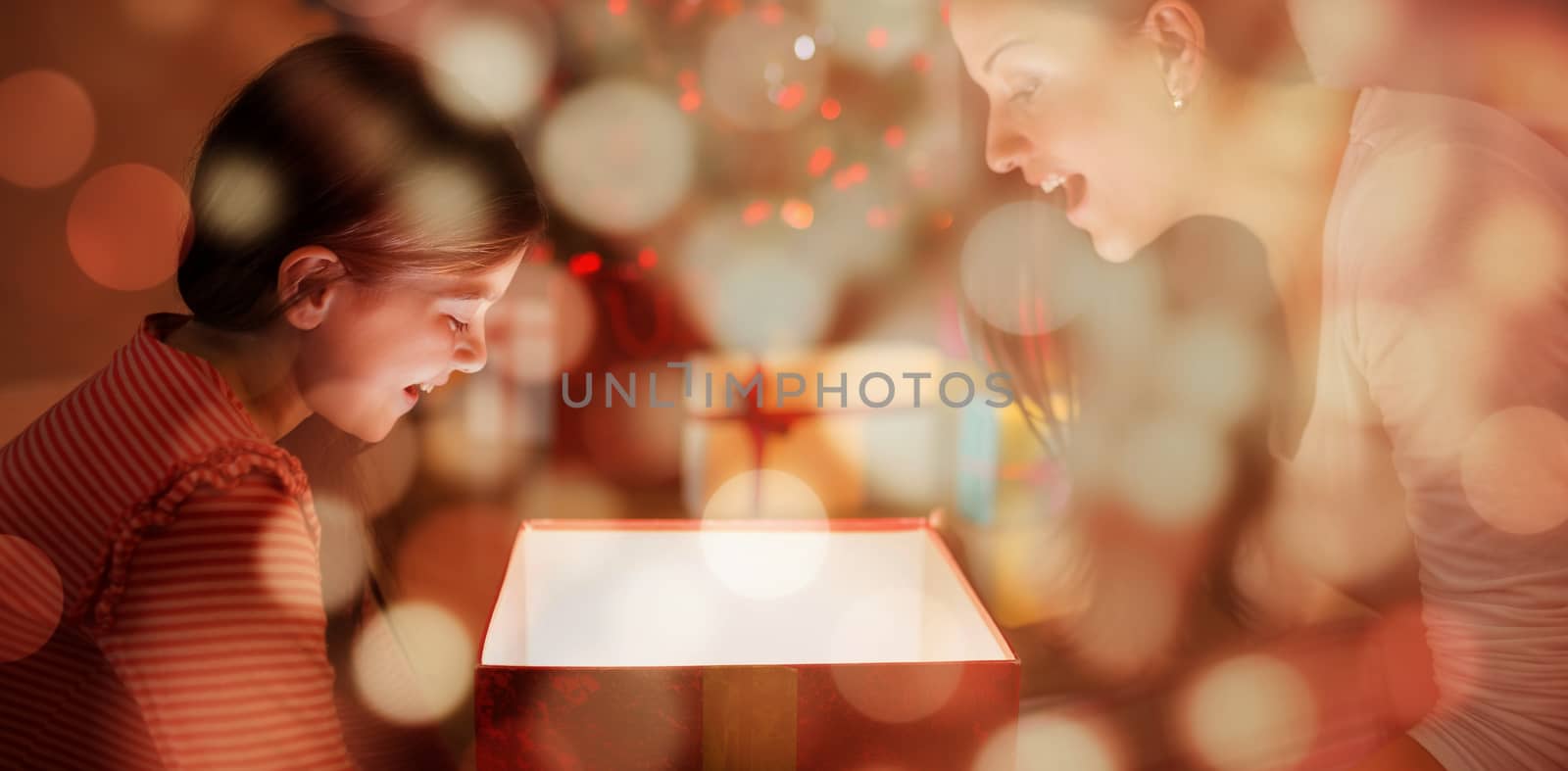 Festive mother and daughter opening a glowing christmas gift against light circles on black background