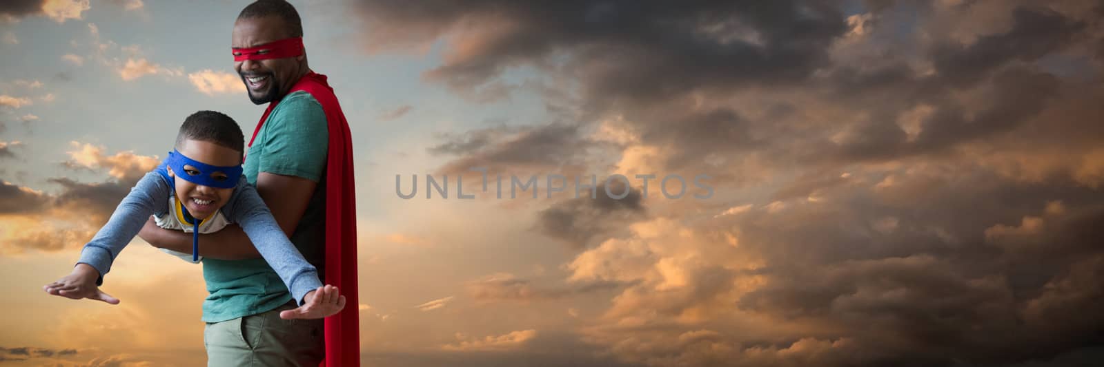 Father and son pretending to be superhero against blue and orange sky with clouds