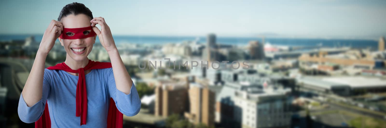 Woman pretending to be superhero against cityscape by sea against blue sky