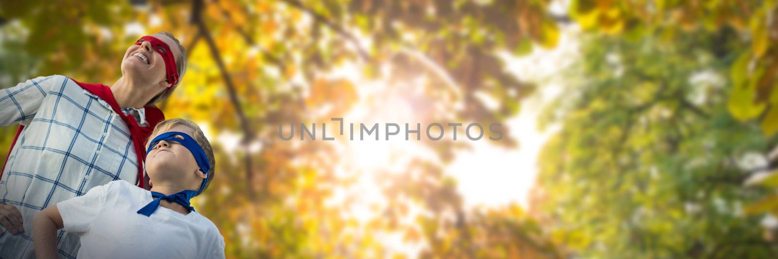 Mother and son pretending to be superhero against low angle view of back lit trees