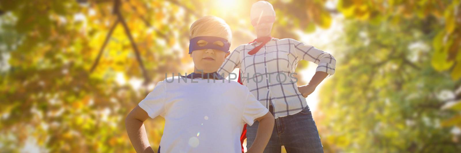 Mother and son pretending to be superhero against low angle view of back lit trees