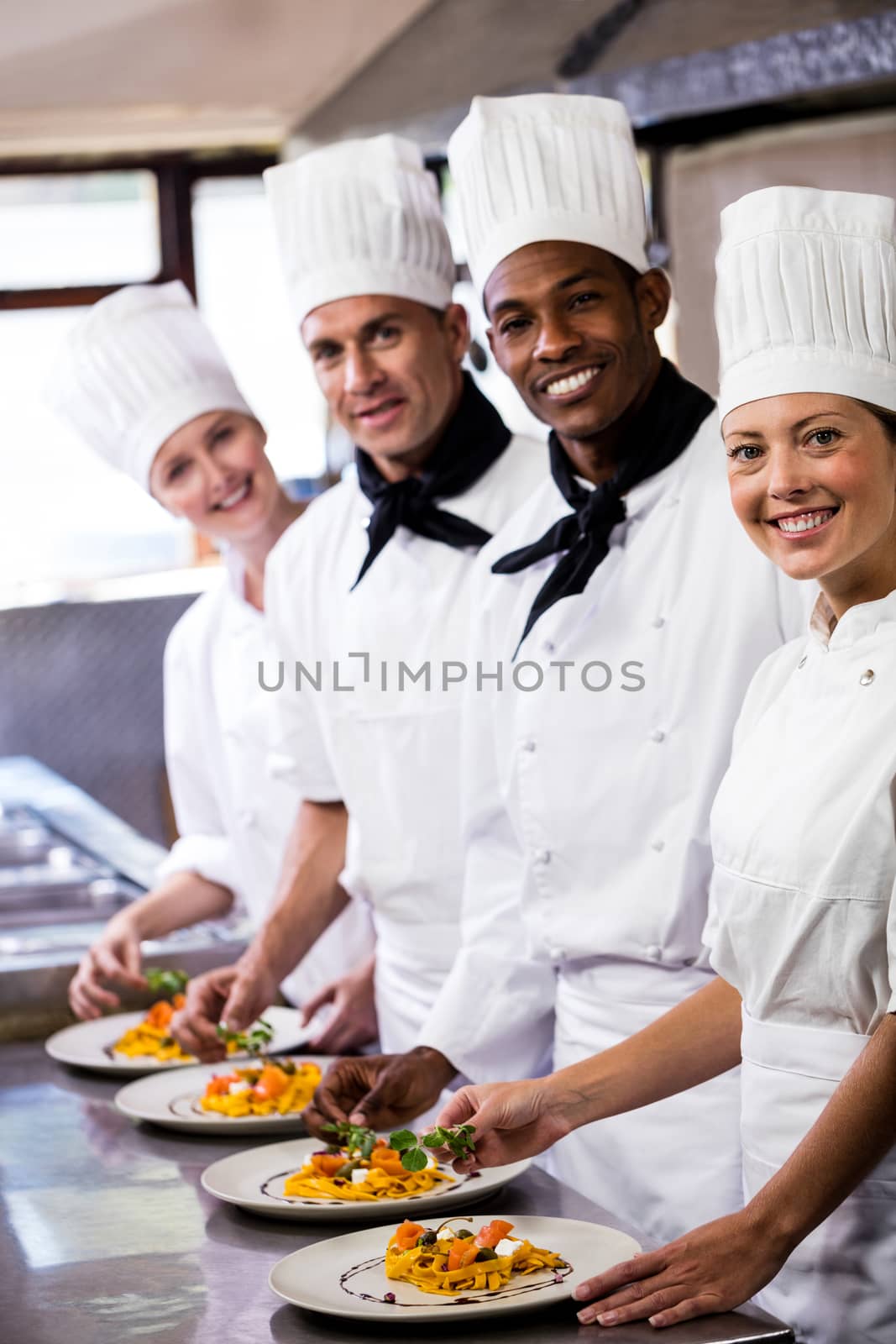 Group of chefs holding plate of prepared pasta in kitchen at hotel