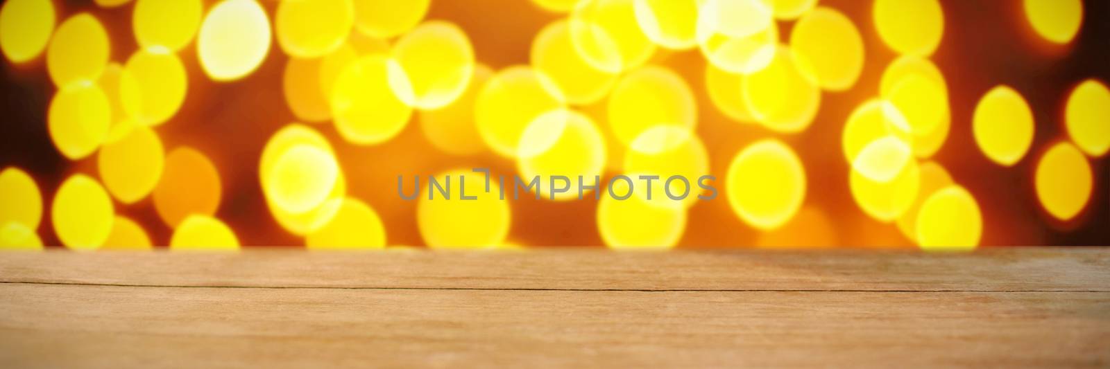 Composite image of wooden table against unfocused yellow christmas light