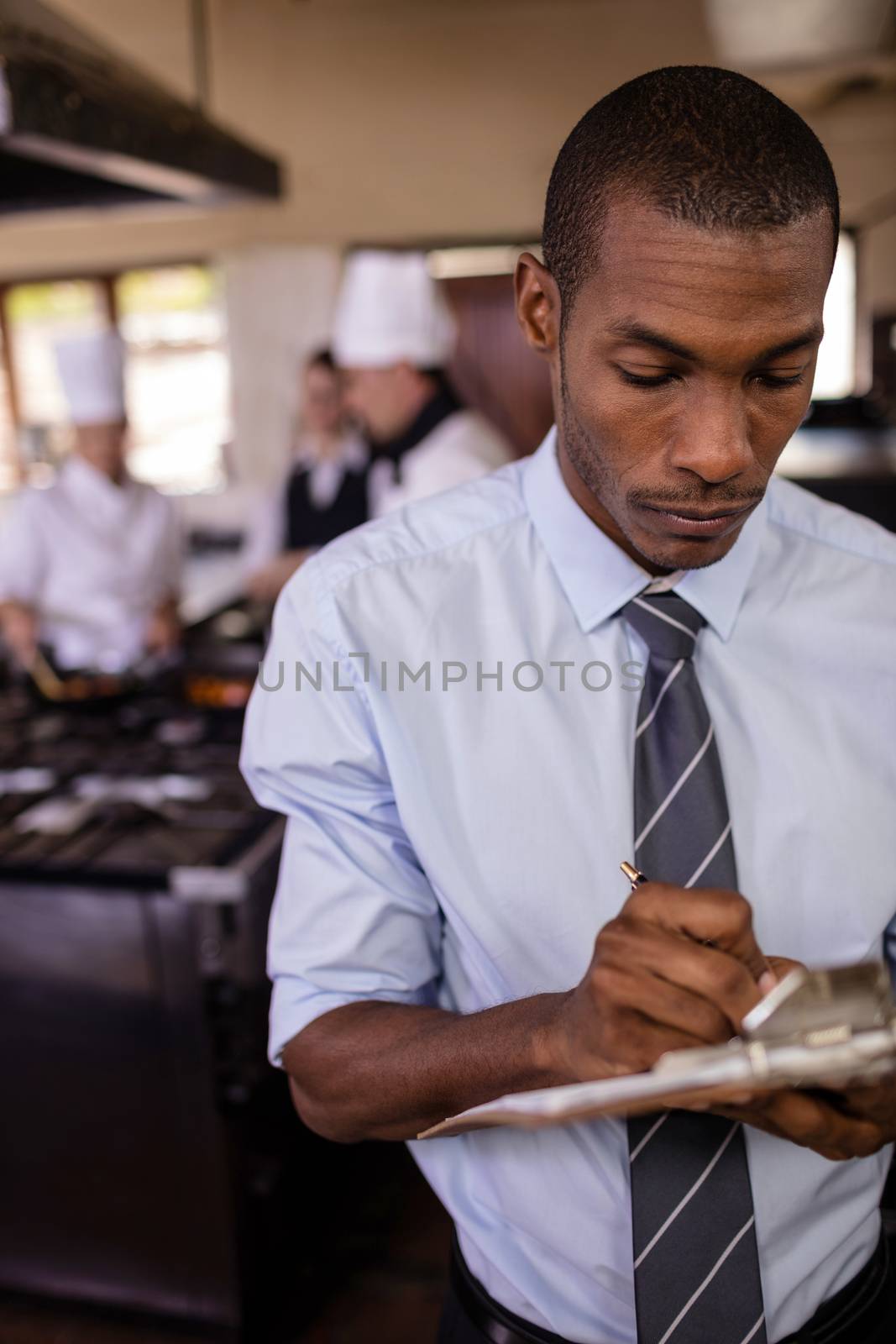 Male manager writing on a clipbaord in kitchen by Wavebreakmedia