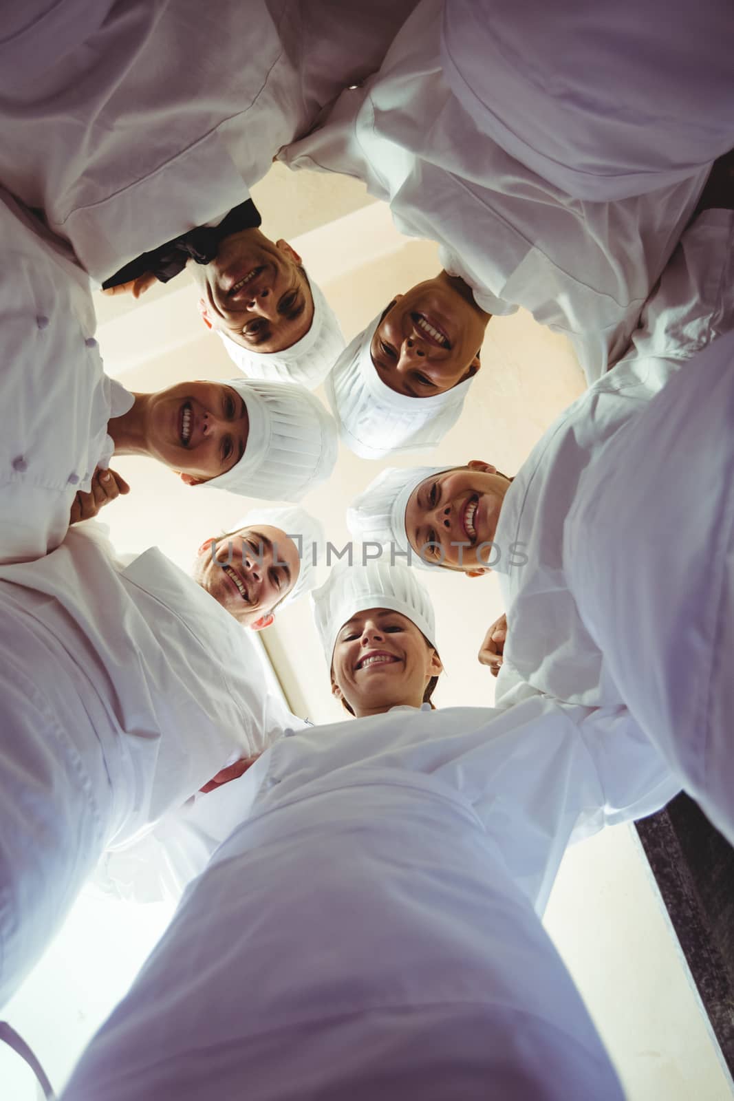 Group of chefs formig huddles in kitchen by Wavebreakmedia