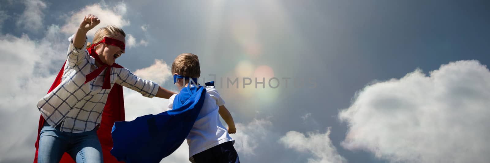 Mother and son pretending to be superhero against cloudy sky with sunshine 