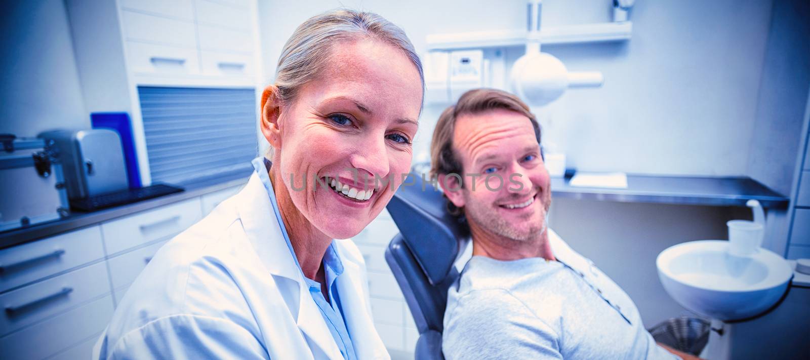 Female dentist writing on clipboard while interacting with male patient in dental clinic