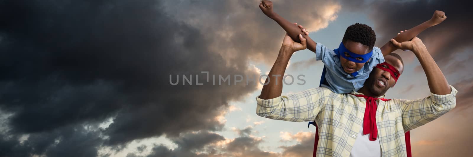 Father and son pretending to be superhero against blue and orange sky with clouds