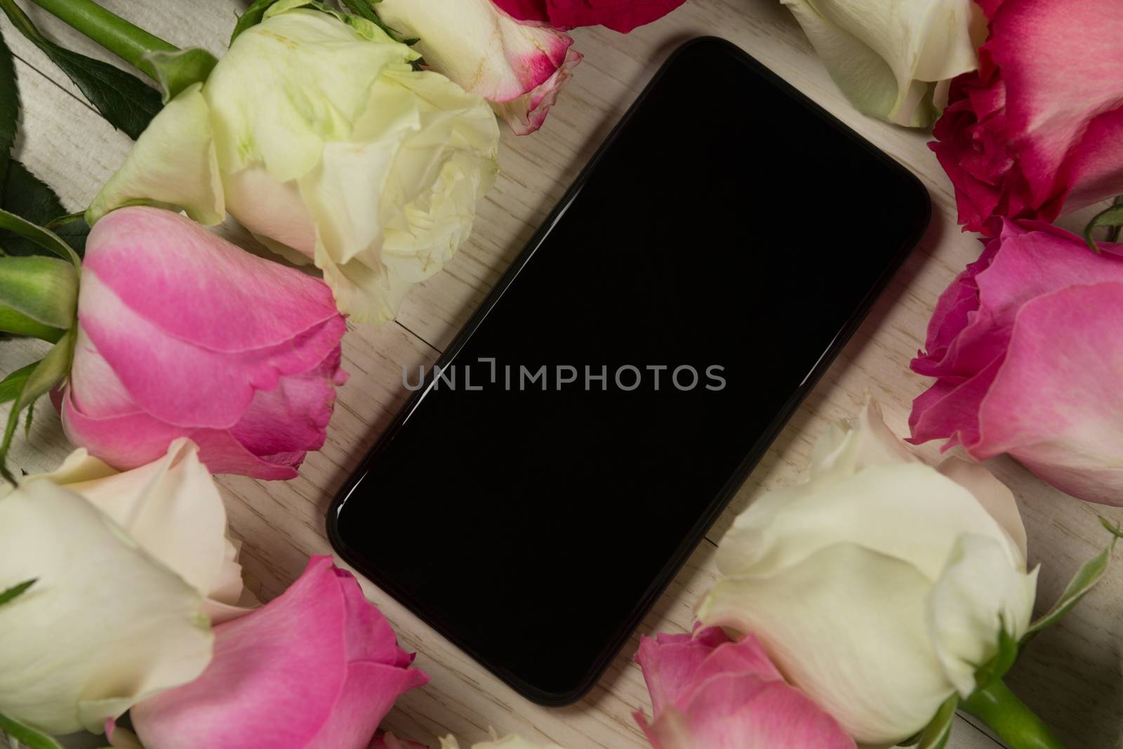 Close-up of mobile phone surrounded with rose flower