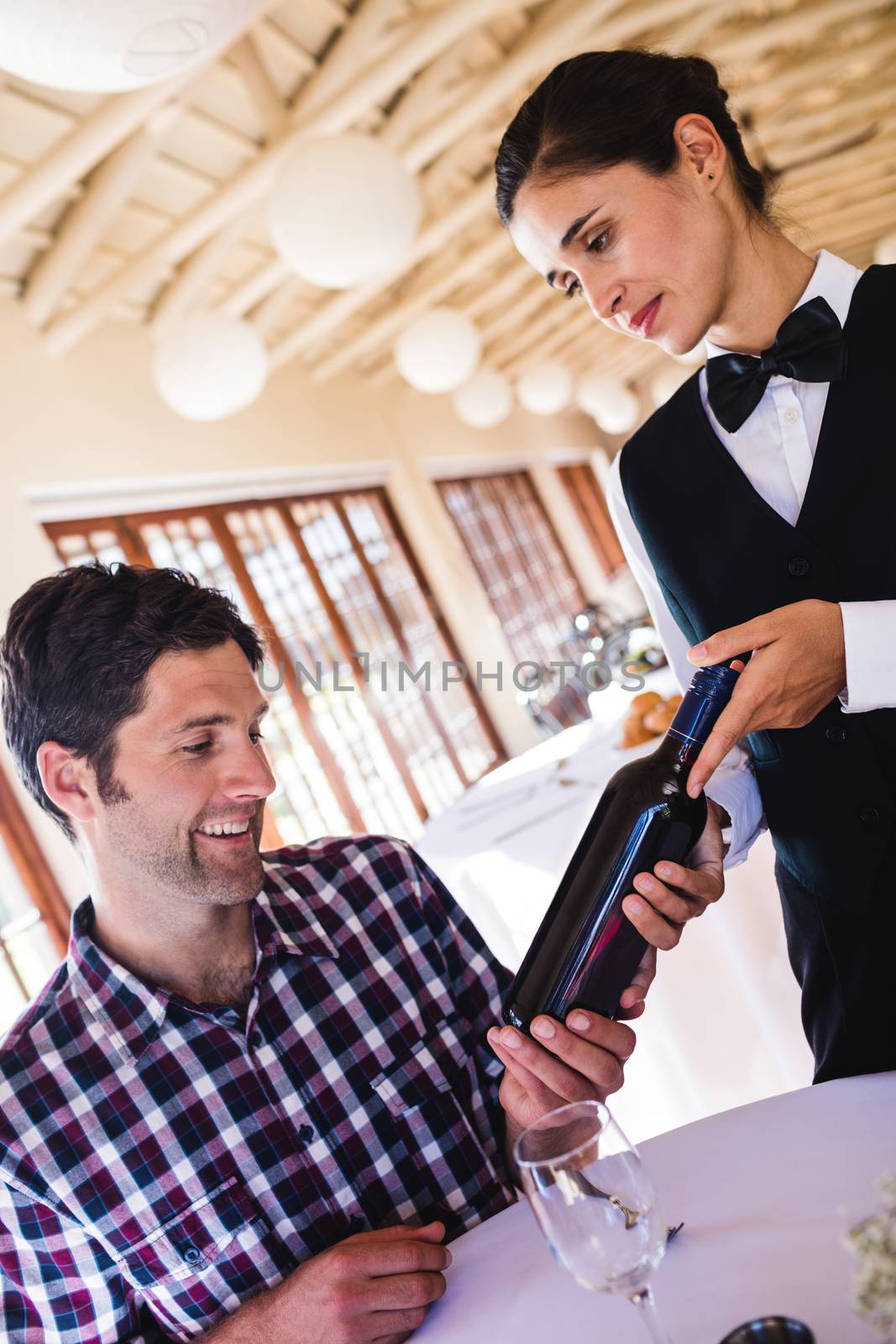 Waitress showing wine to customer at table by Wavebreakmedia