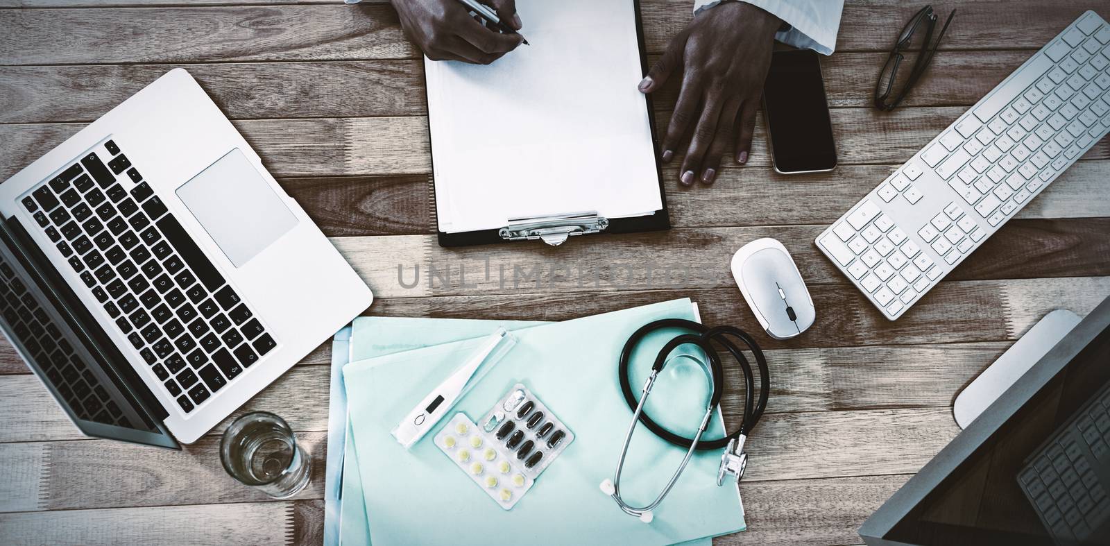 Cropped hand of doctor writing on clipboard at desk