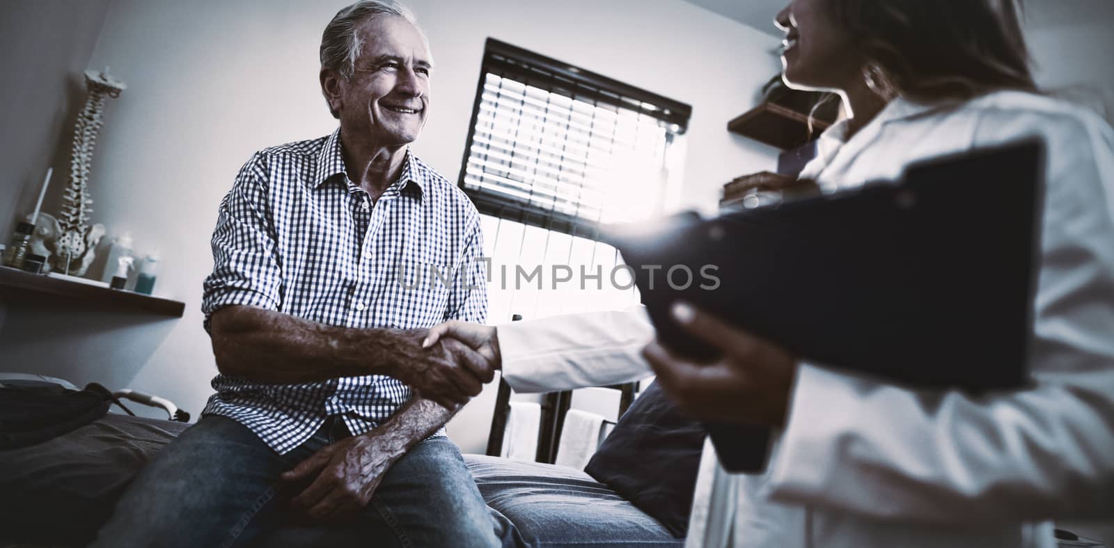 Low angle view of female therapist and senior male patient shaking hands at hospital ward