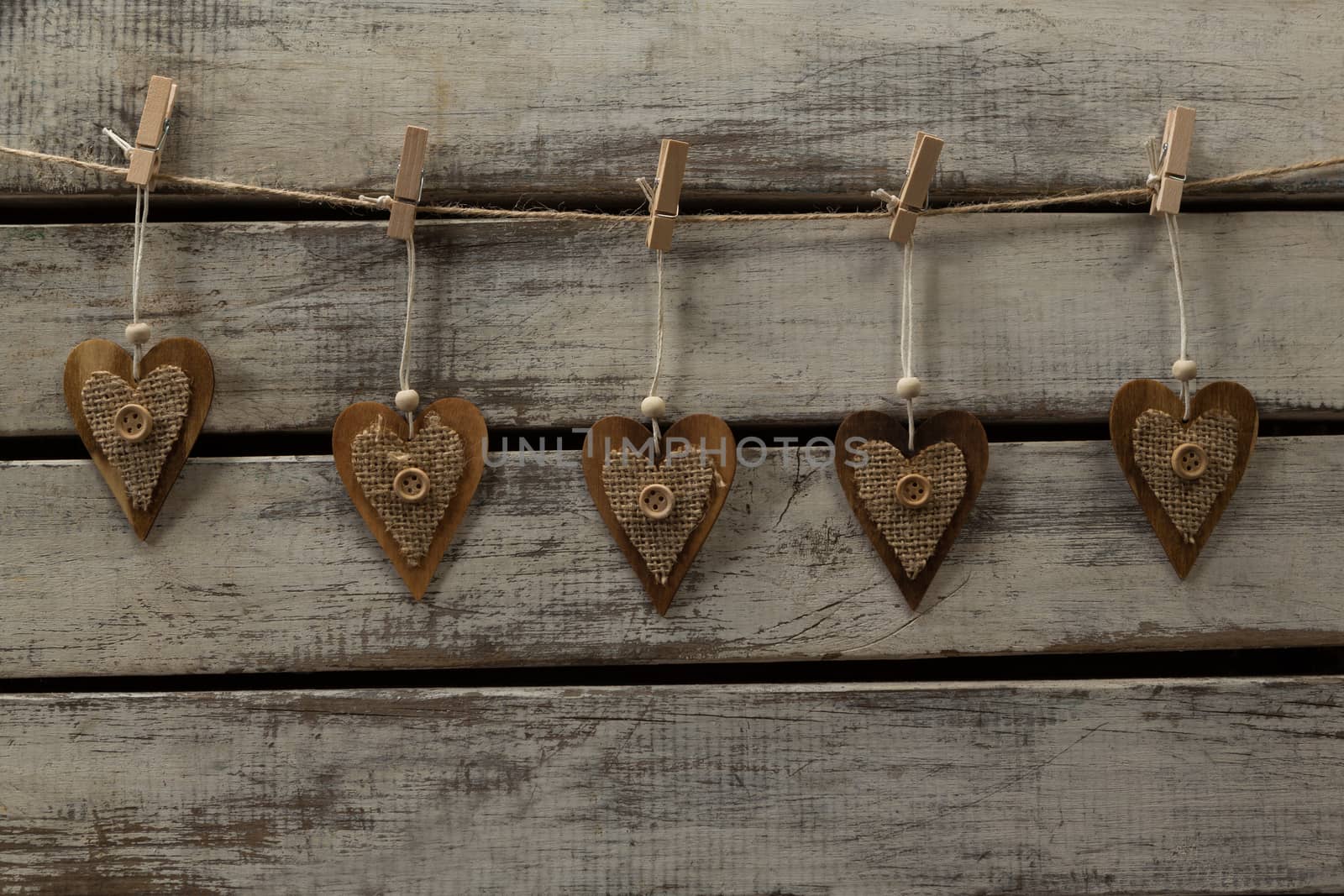 Heart shape decorations hanging on thread against wooden plank