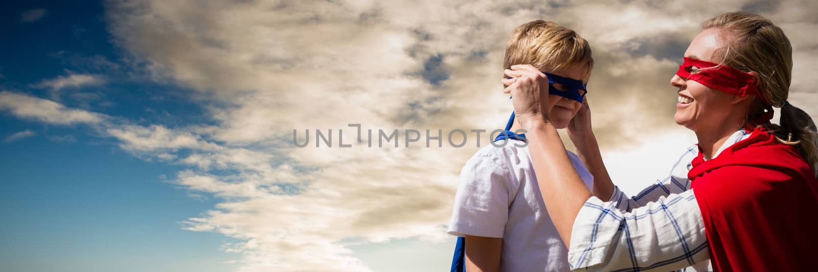 Mother and son pretending to be superhero against cloudy sky over countryside