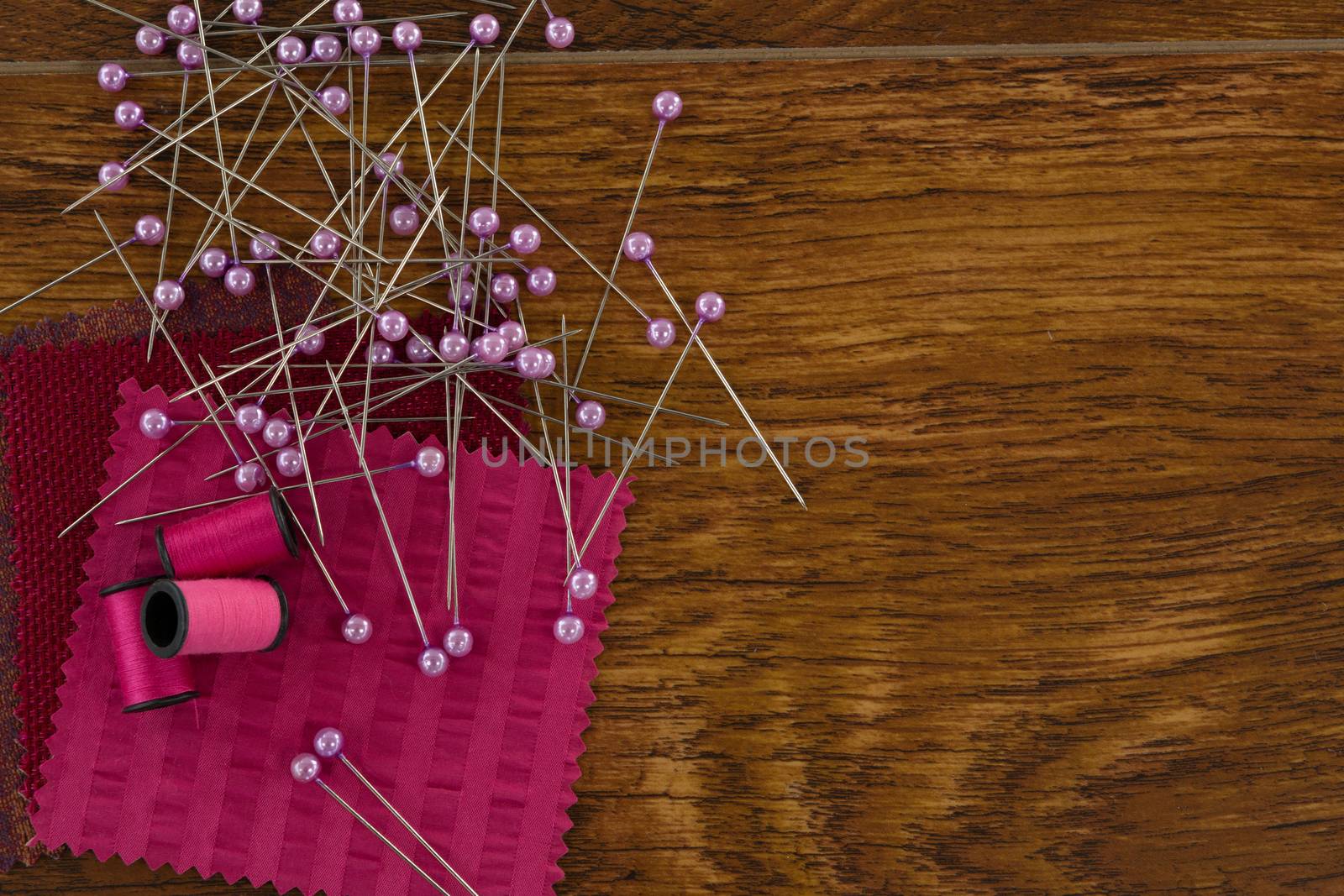Thread rolls, sewing pins and textile on wooden table