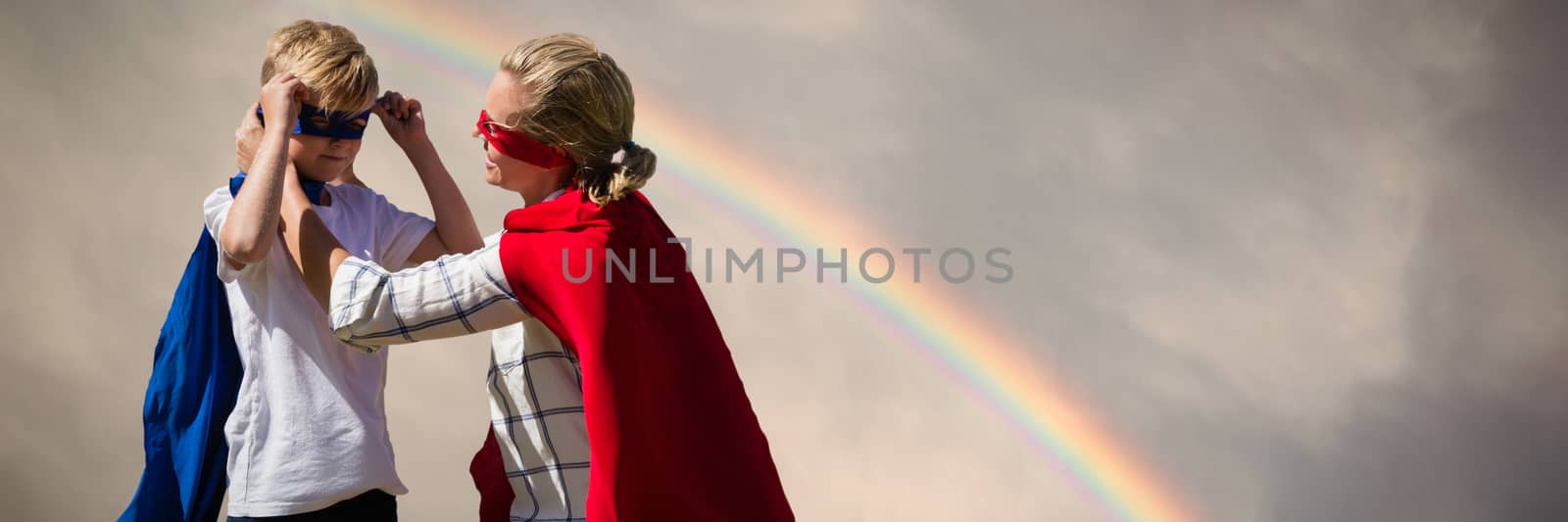 Mother and son pretending to be superhero against rainbow in a dark sky above the green hill