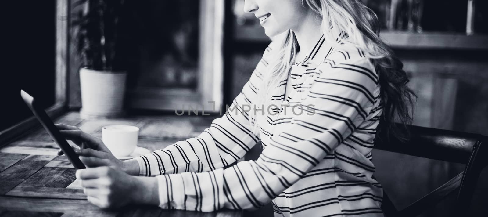 Smiling woman using digital tablet while having coffee in cafÃ©