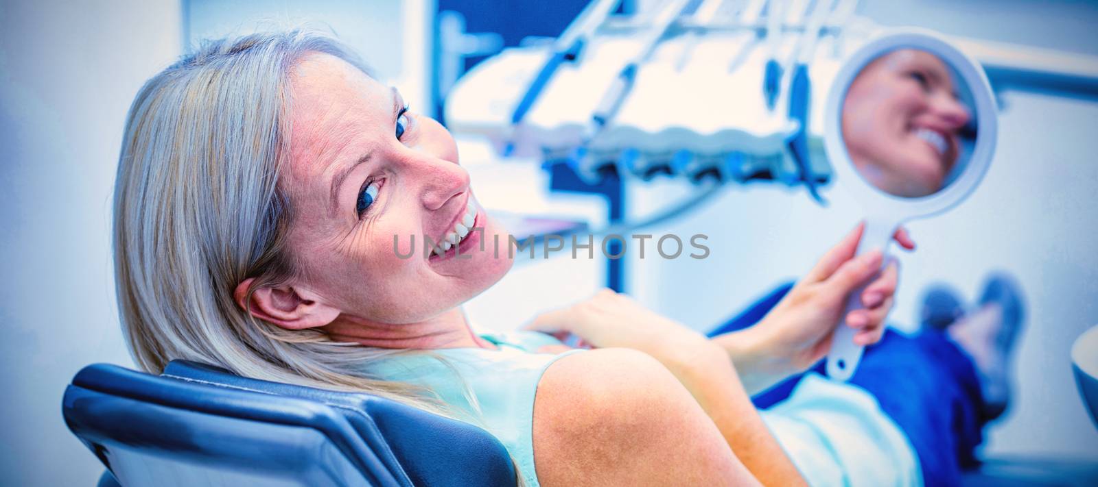 Female patient smiling while holding mirror in dental clinic