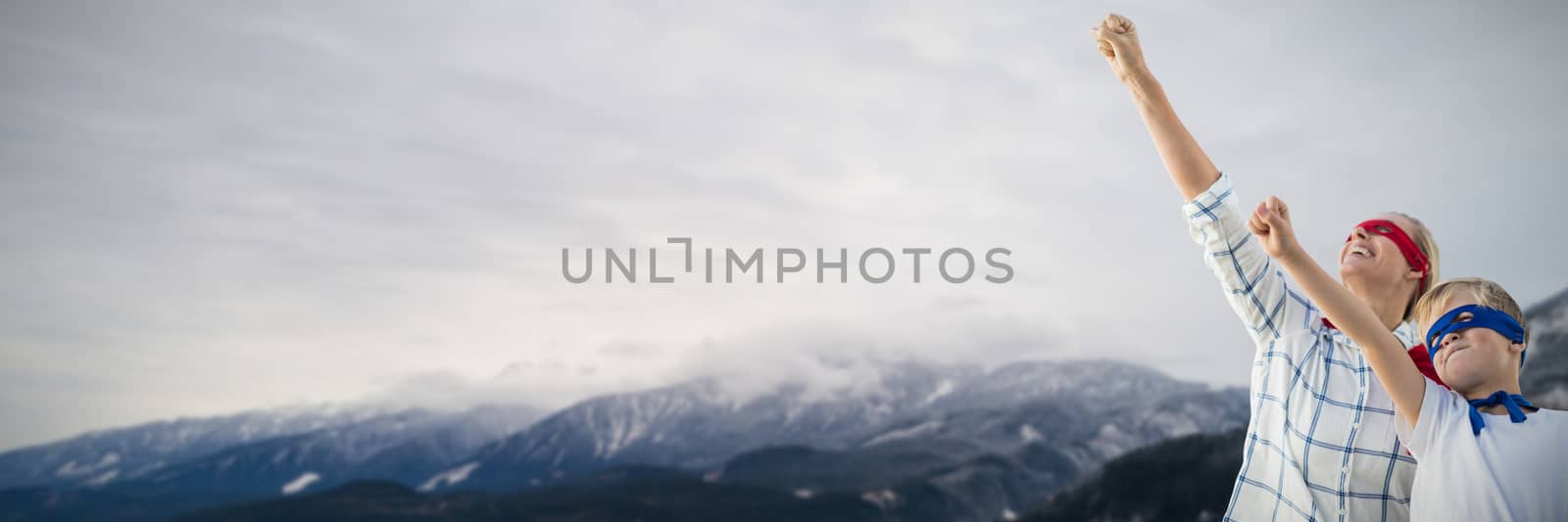 Mother and son pretending to be superhero against coniferous trees on snowy landscape surrounded with mountains