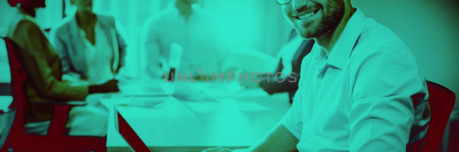 Portrait of man using laptop while coworker interacting in the background in the office