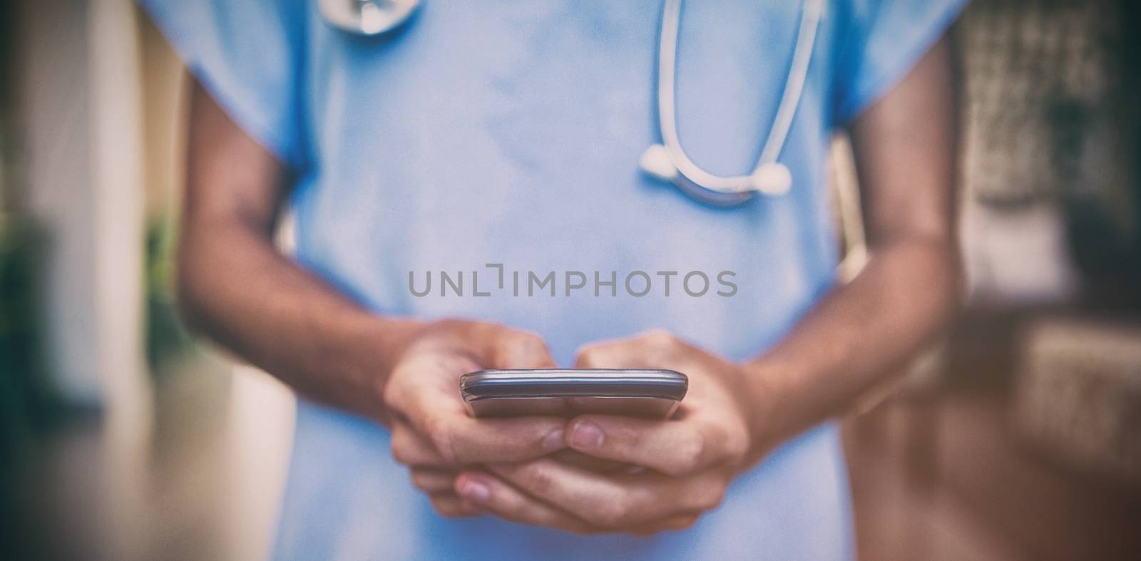 Mid-section of doctor using mobile phone in hospital