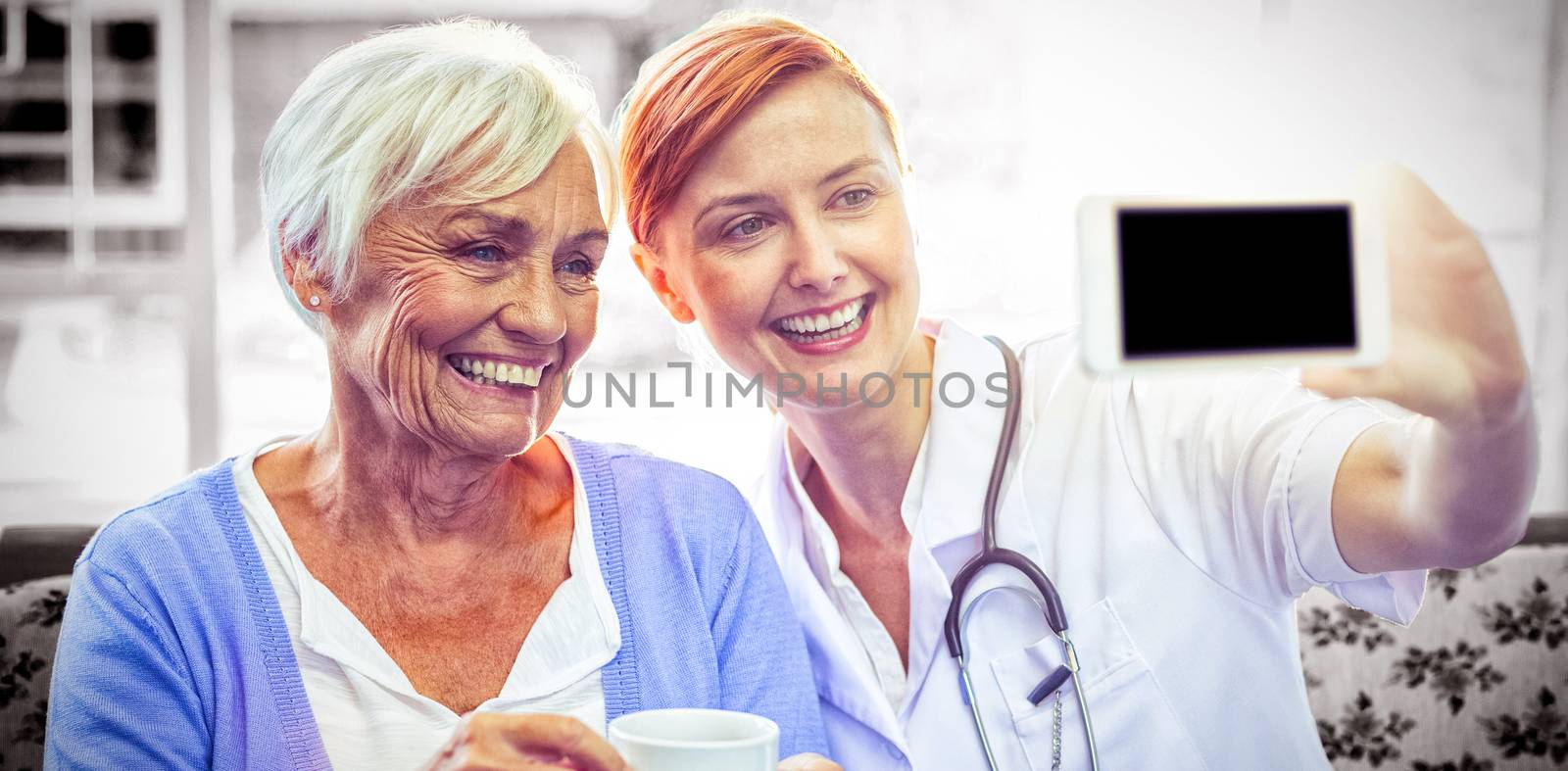 Smiling doctor and patient looking at phone while having tea at home