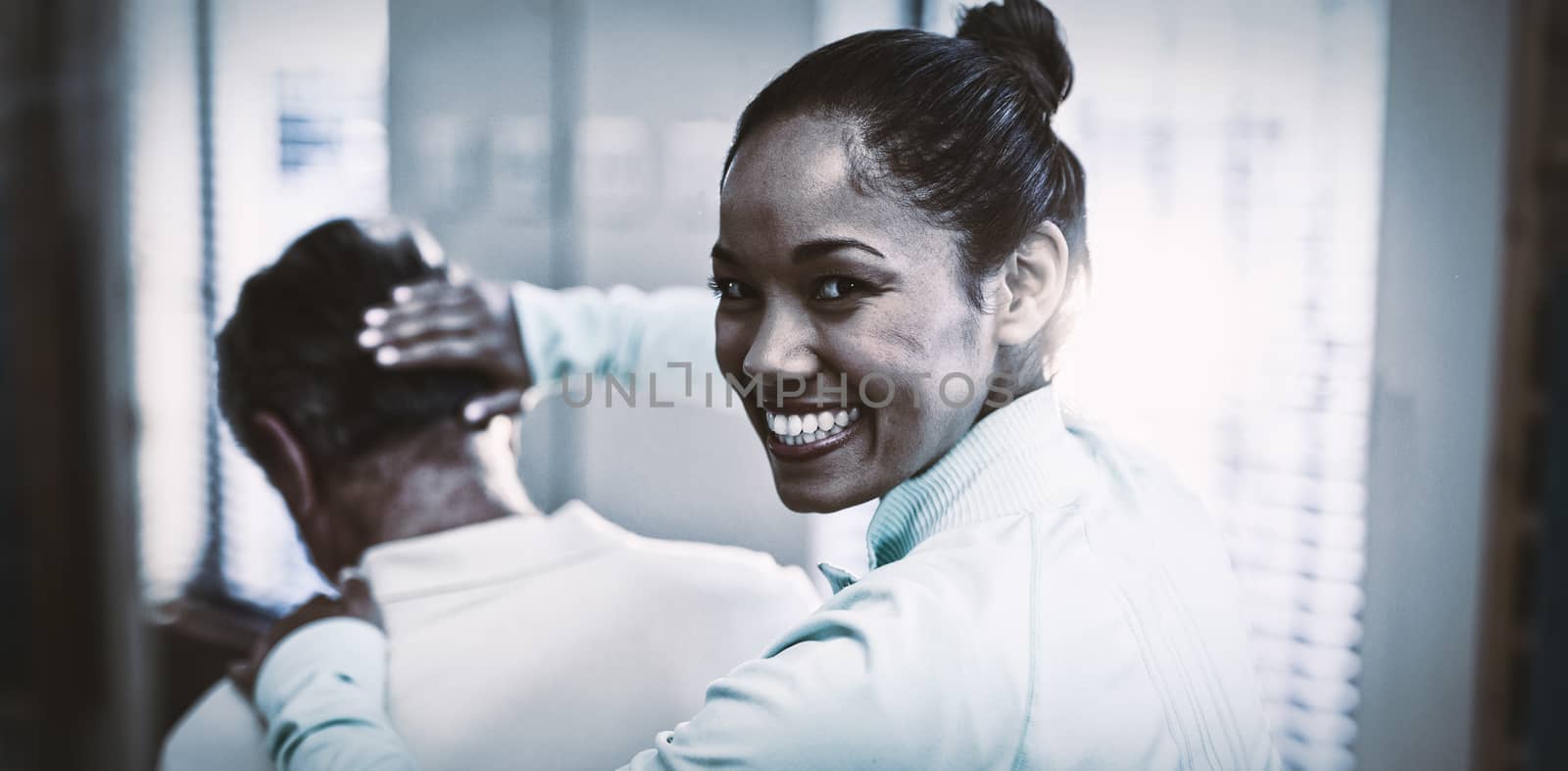 Rear view of portrait of smiling female therapist giving neck massaging to senior male patient at hospital ward