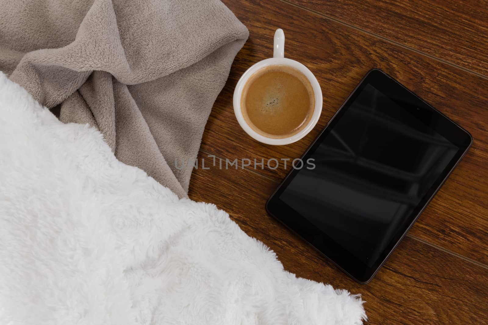 Close-up of digital tablet with blanket and coffee on wooden background