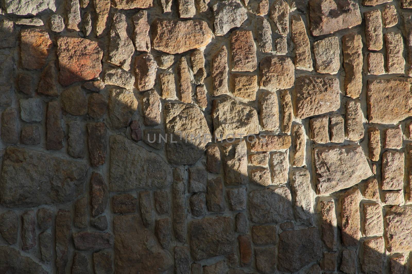 Dry stone wall texture background, in searing light and diagonal shadow.