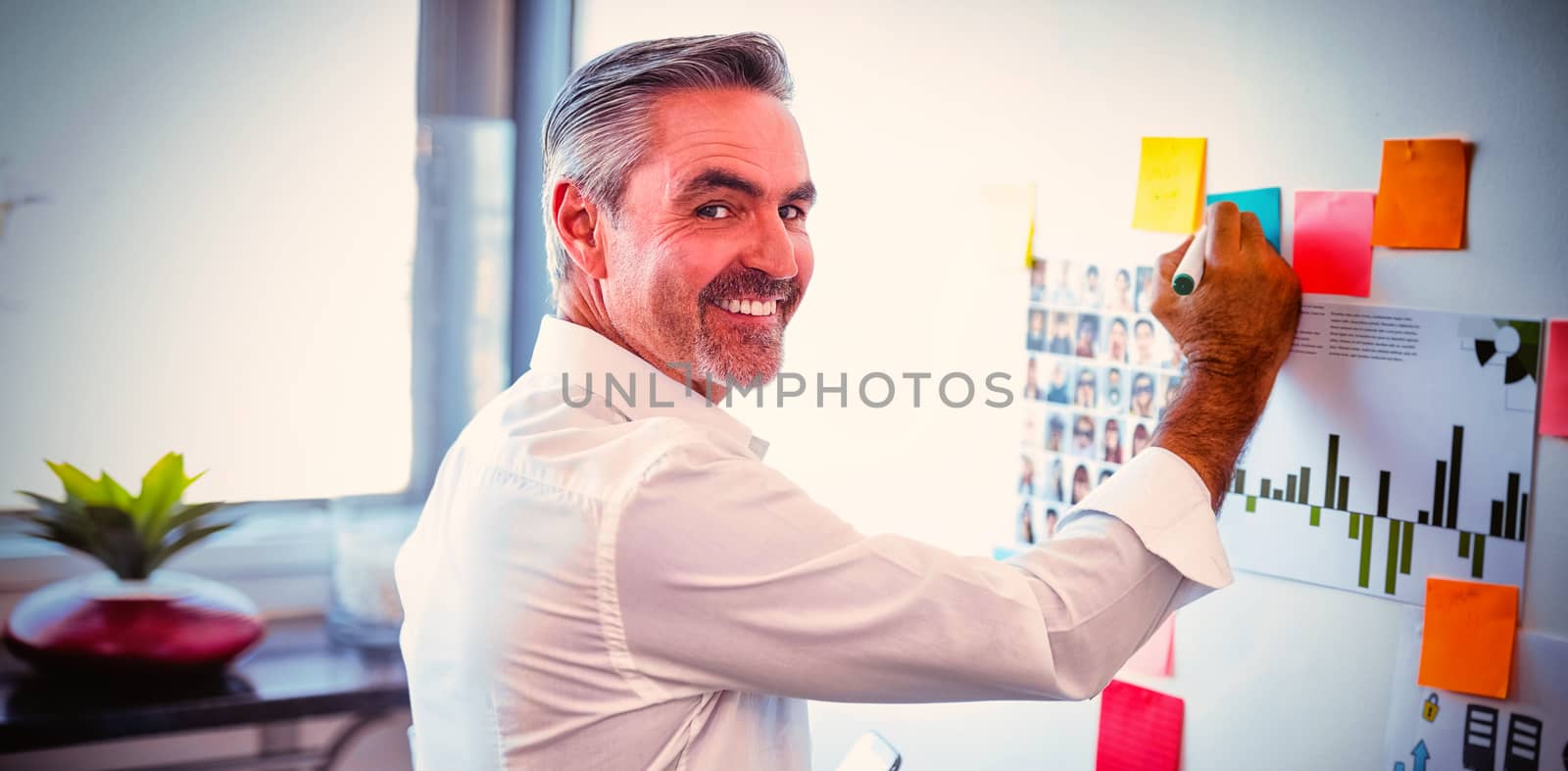 Portrait of happy mature businessman making strategies on whiteboard in creative office