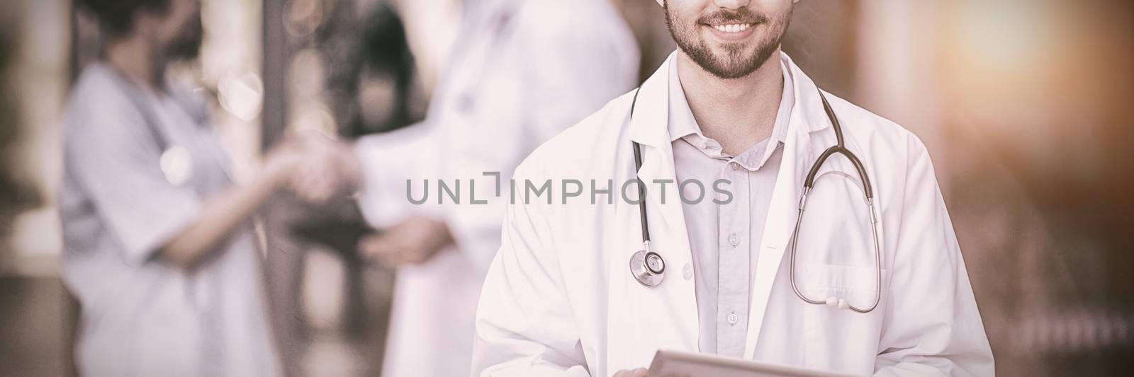 Portrait of smiling doctor standing with digital tablet in hospital