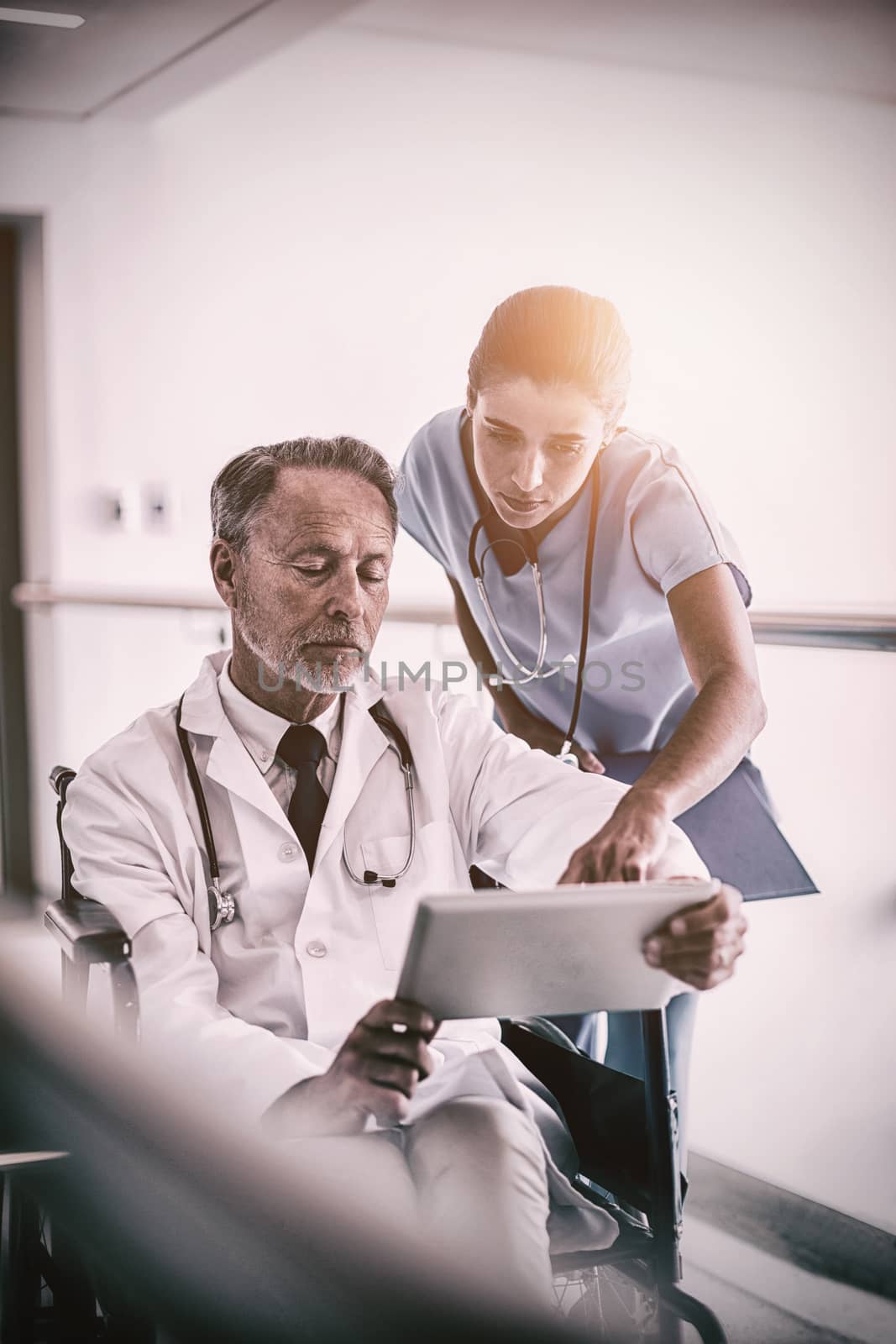 Male doctor with nurse talking over digital tablet in hospital