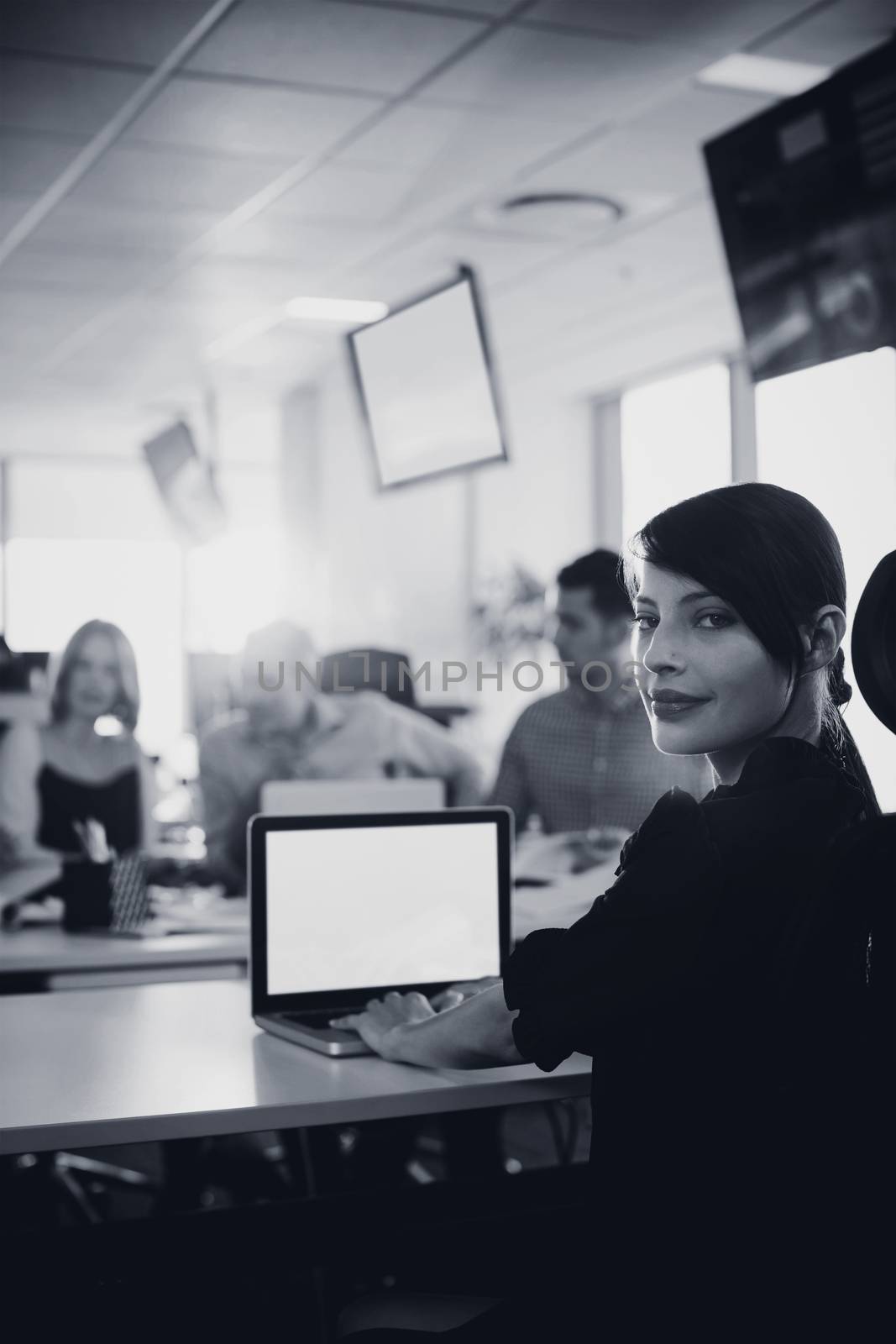Portrait of young businesswoman working on laptop at desk in office