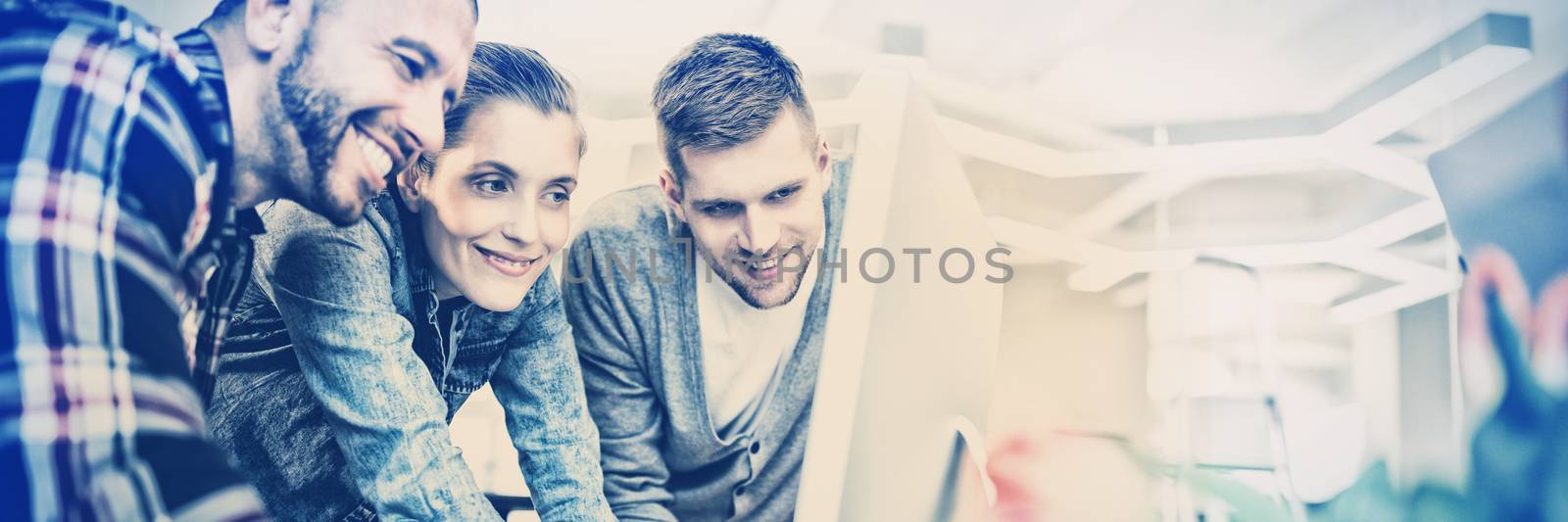 Smiling business people looking at computer in creative office